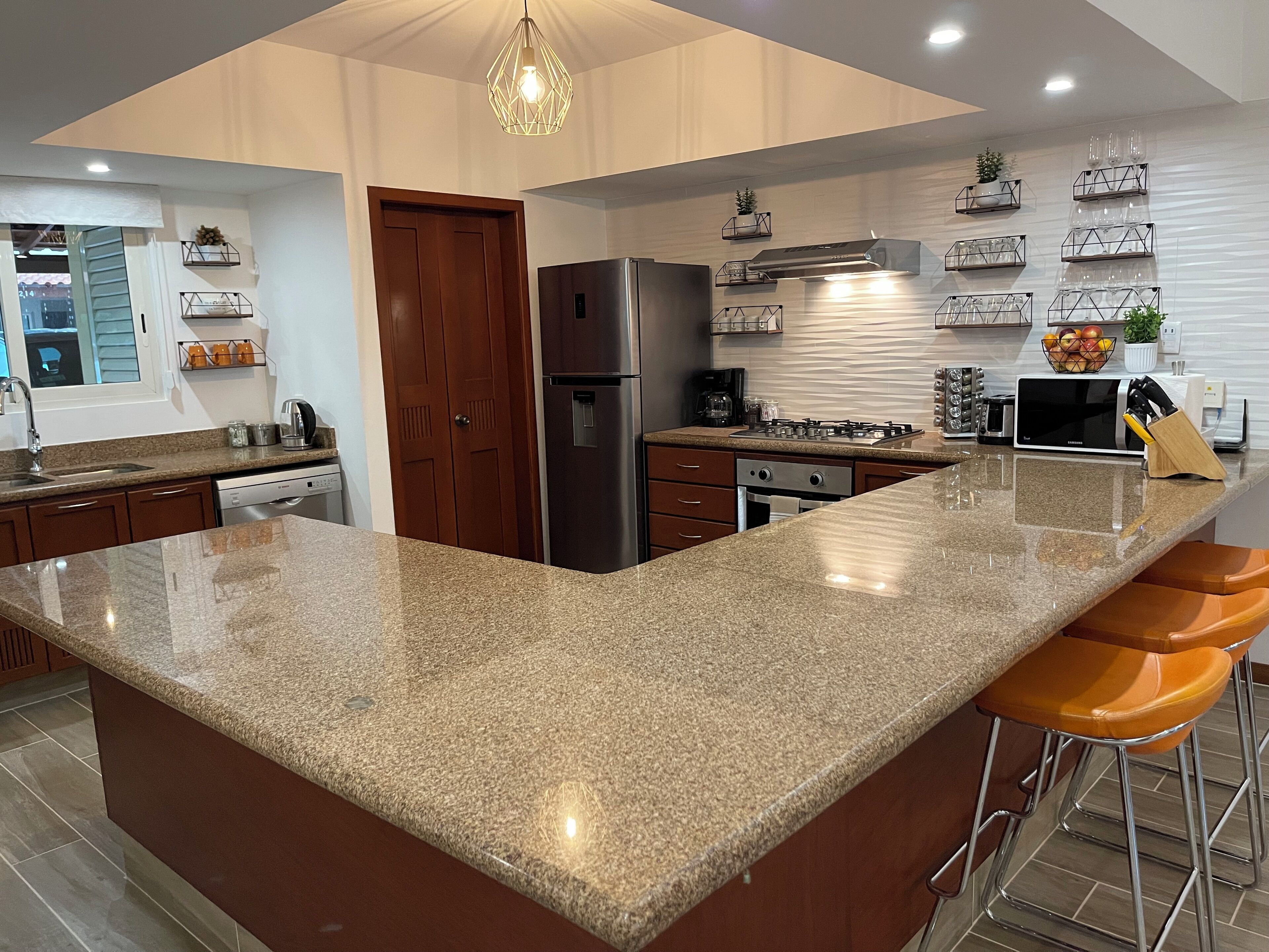 A modern kitchen with granite countertops, stainless steel appliances, and bar stools.
