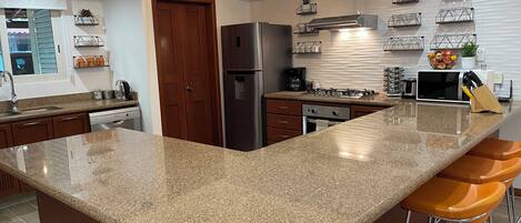 A modern kitchen with granite countertops, stainless steel appliances, and bar stools.