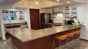 A modern kitchen with a large island, bar stools, stainless steel appliances, and a decorative light fixture. - Poolside Condo, El Tigre. Beautiful (Nuevo Vallarta)