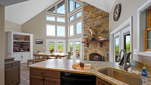Una cocina amplia con chimenea de piedra, ventanas grandes y un aparador para café y vinos.