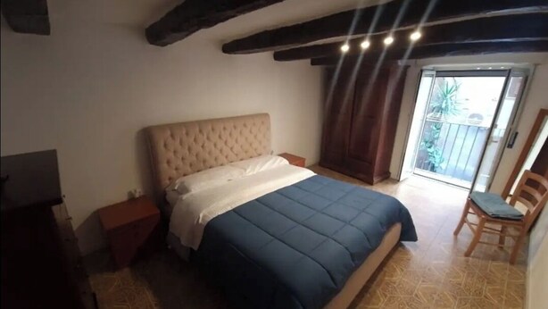 Un dormitorio con una cama grande, una mesita de noche de madera, una silla y vistas al exterior a través de una puerta corredera.