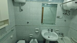 Un baño con inodoro, bidé, dos lavamanos y ducha.
