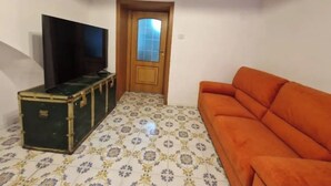 Una habitación con piso estampado, una puerta de madera, una maleta verde y un sofá naranja.