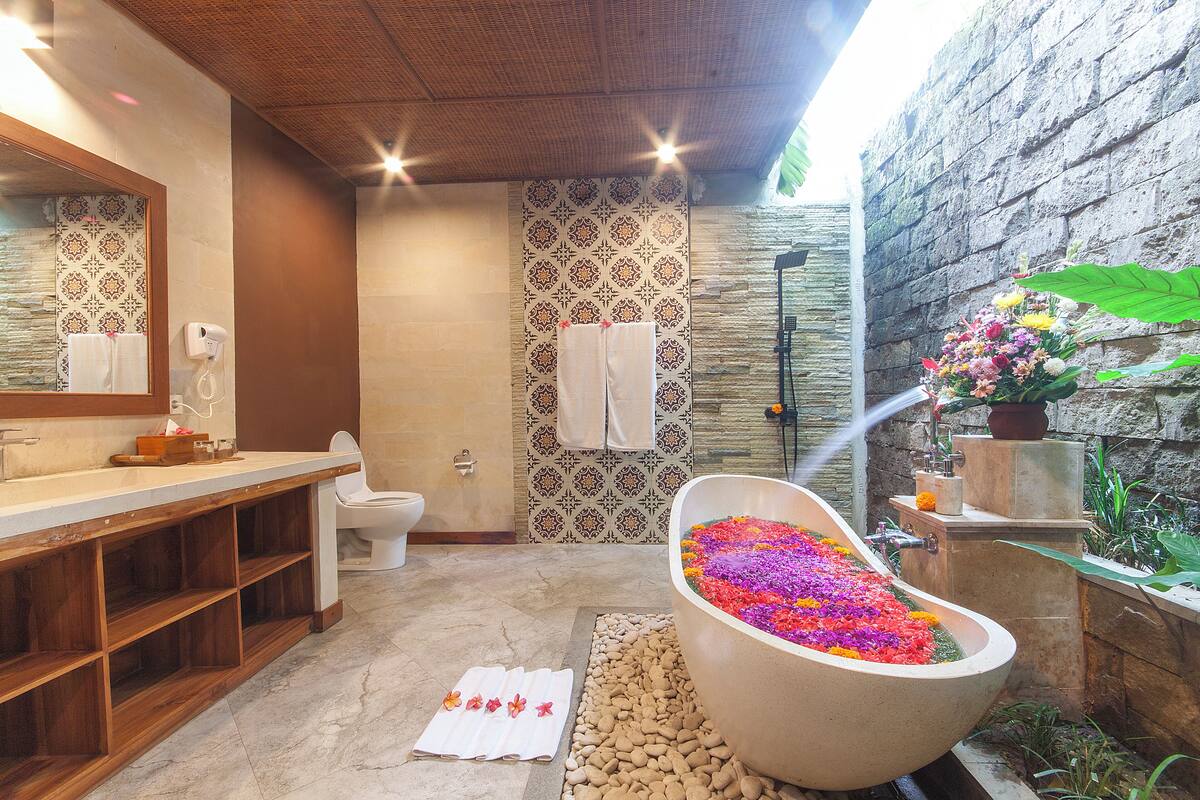 Une salle de bain avec une grande baignoire remplie de fleurs colorées, un meuble-lavabo en bois, des toilettes et un espace douche.