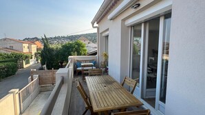 Een balkon met een houten tafel en stoelen, een schuifdeur en uitzicht op de omgeving.