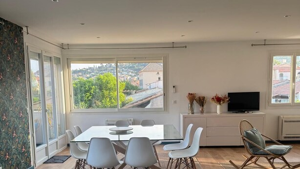 Een moderne eetruimte met een glazen tafel, witte stoelen en uitzicht op een heuvel.