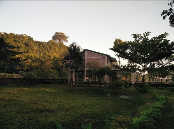 A modern building with a brick facade and a flat roof, surrounded by a grassy area and trees. - Neelima Resort (Cox's Bazar)