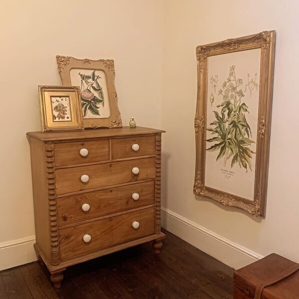 A wooden dresser with drawers against a wall, accompanied by two framed botanical illustrations.