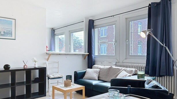 A modern living room with a sofa, a small table, and a dining area with a checkered tablecloth.
