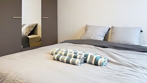 A neatly made bed with a striped blanket, a grey and white pillow, and a grey duvet.
