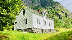 Een wit houten huis met een stenen fundering, gelegen aan een groene heuvel.