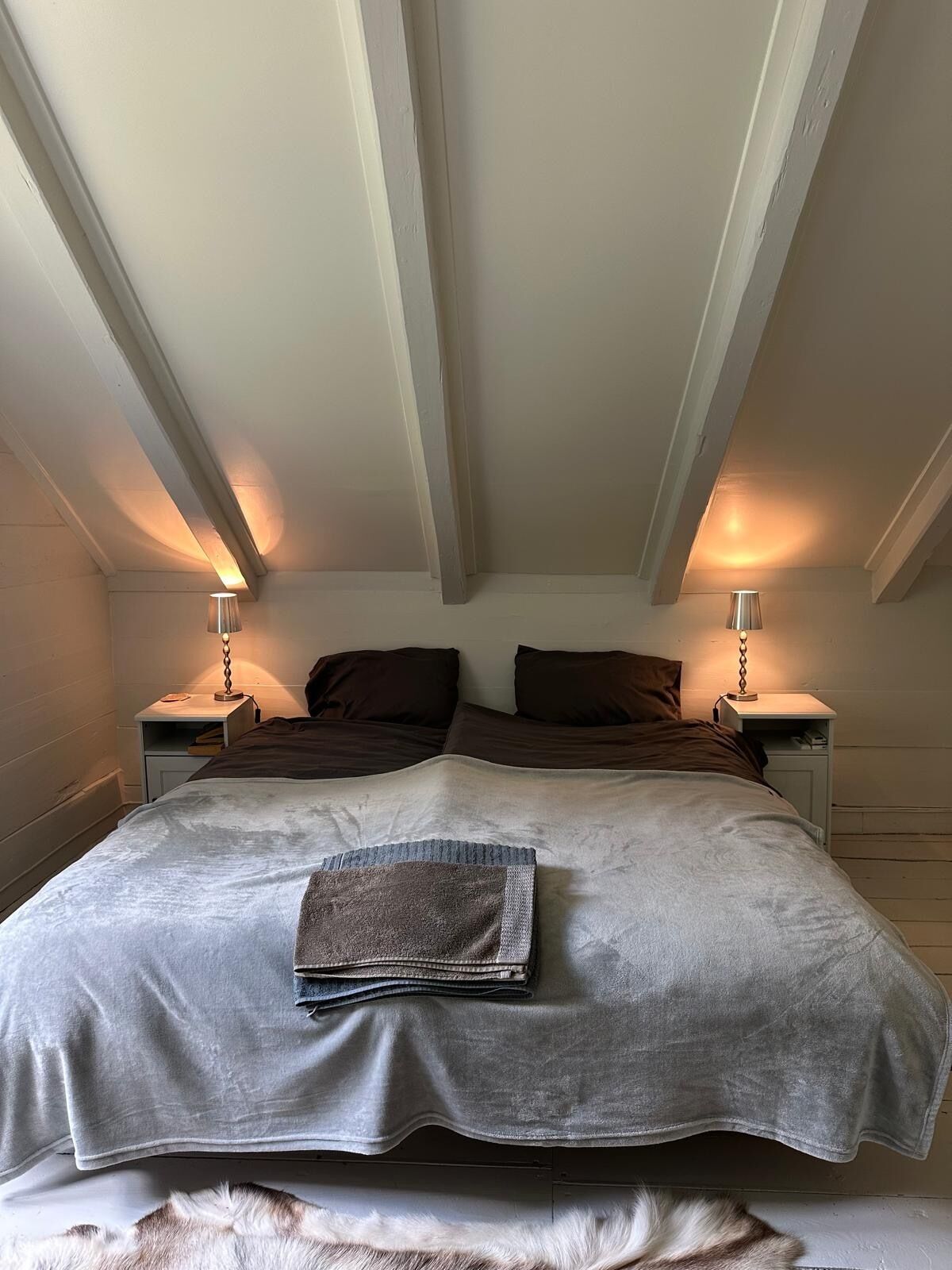 Ein Schlafzimmer mit einem großen Bett, zwei Nachttischen mit Lampen und einer Decke mit sichtbaren Holzbalken.