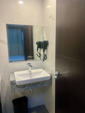 Une salle de bain avec un lavabo blanc, un miroir et deux sèche-cheveux fixés au mur.