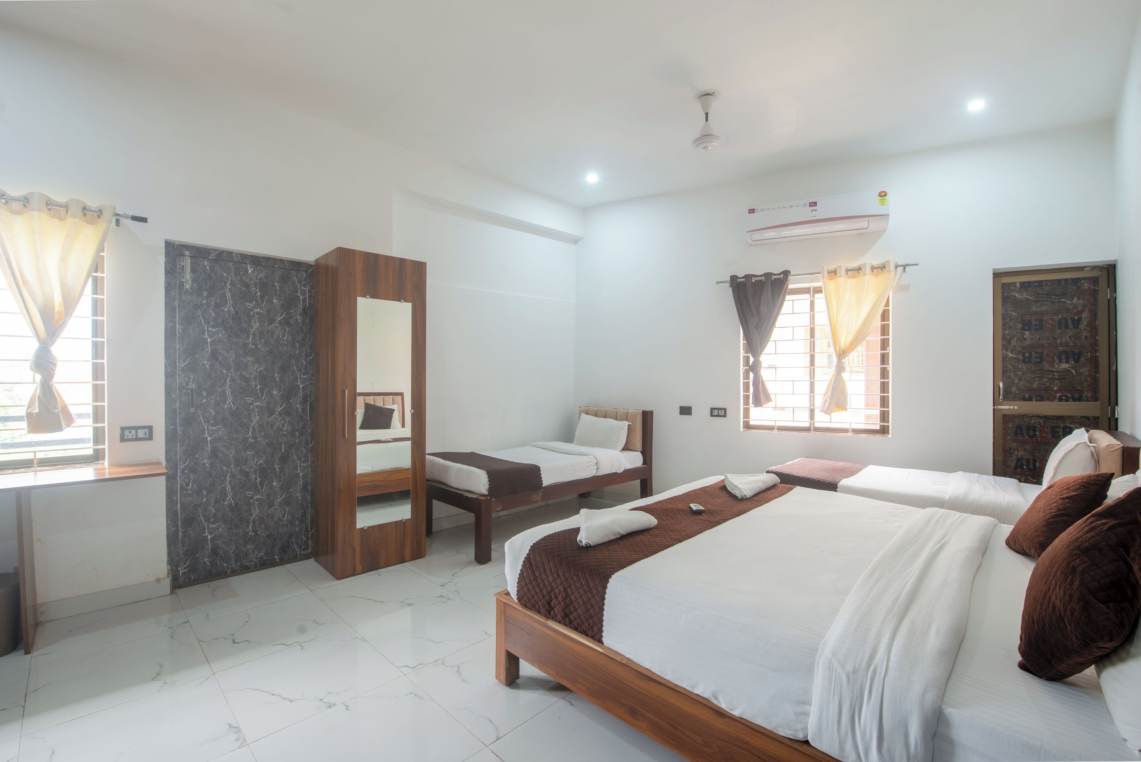 A hotel room with a bed, a desk, a chair, a wardrobe, and a window with curtains.
