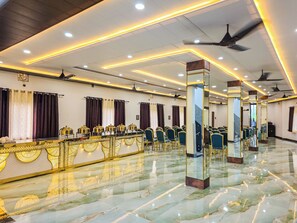 A spacious hall with rows of chairs, a marble floor, and ceiling fans. - Maya's Nest (Varanasi)