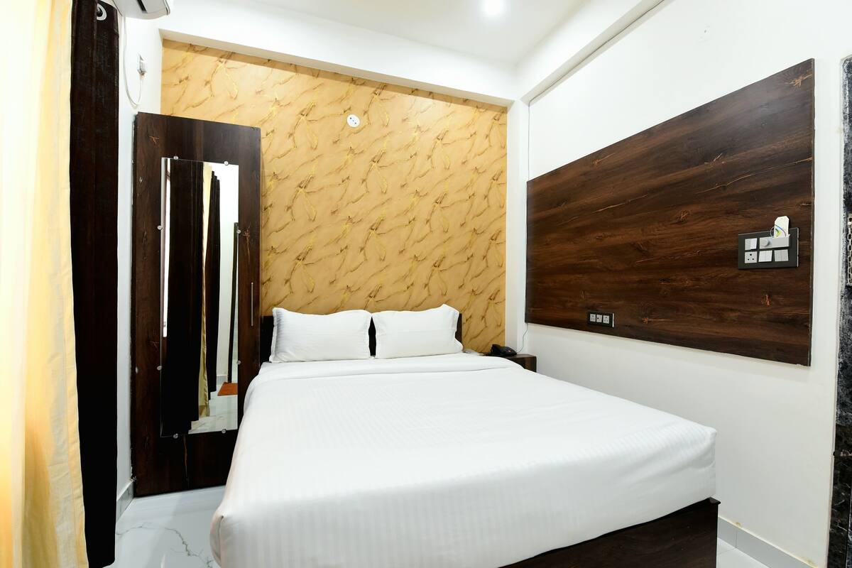 A hotel room with a large bed, a wooden headboard, a mirror, and a wall-mounted power outlet.