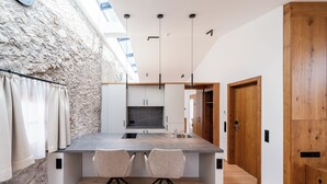 A modern kitchen with a large island, two chairs, and a stone wall. - Hotel Traube Rattenberg (Rattenberg)