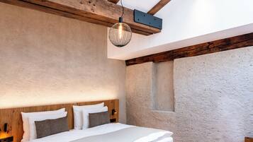 Une chambre dotée d’une lucarne, de poutres en bois, d’un lit avec du linge de lit blanc et d’un mur à texture.