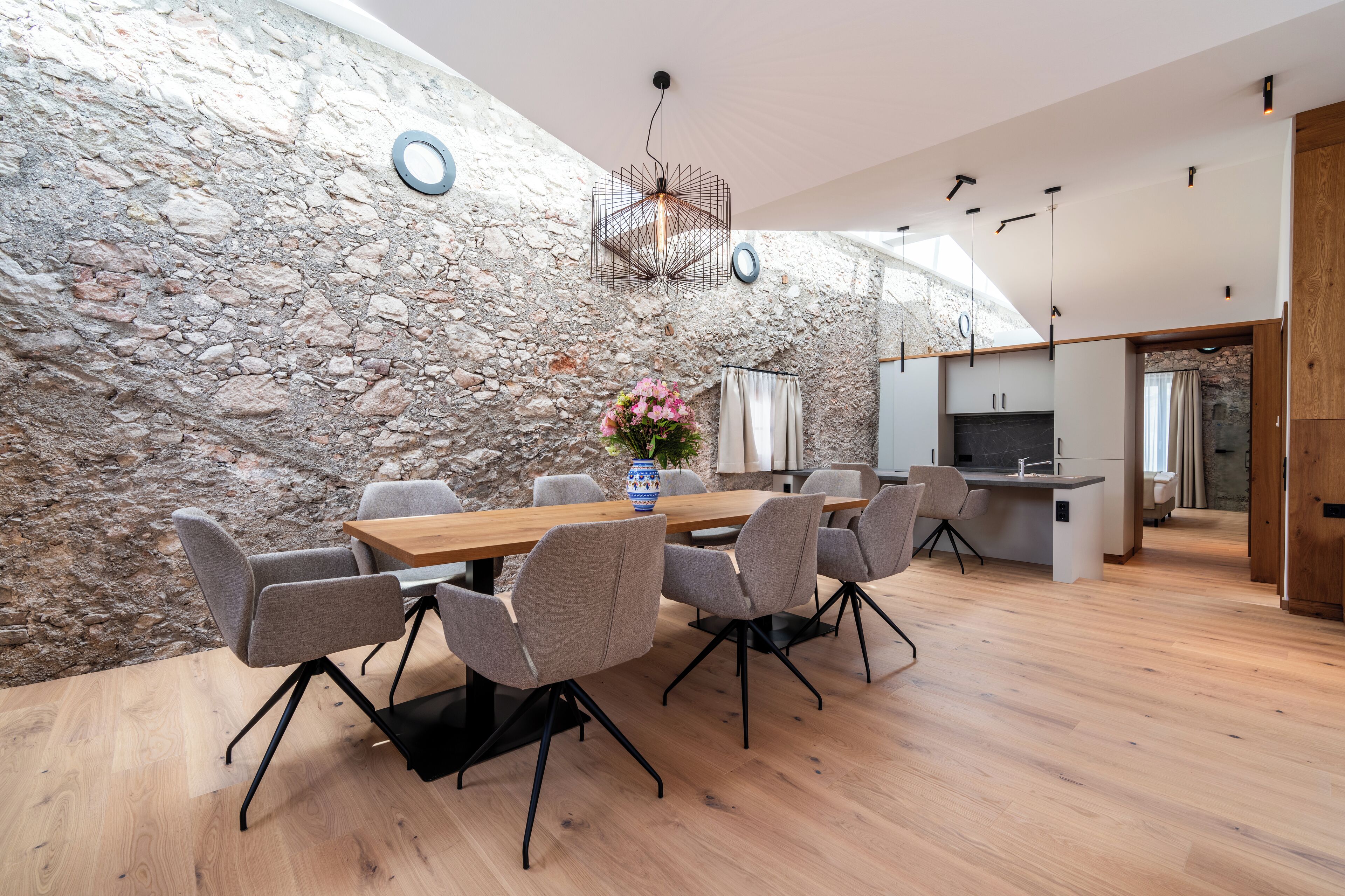Ein stilvoller Essbereich mit Steinwand, Holztisch und grauen Stühlen.