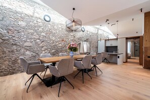 A modern dining area with a stone wall, a wooden table, and grey chairs. - Hotel Traube Rattenberg (Rattenberg)