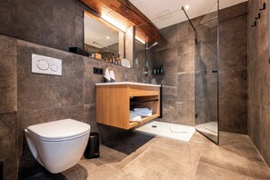 A modern bathroom with a toilet, wooden vanity, glass shower enclosure, and a large mirror.