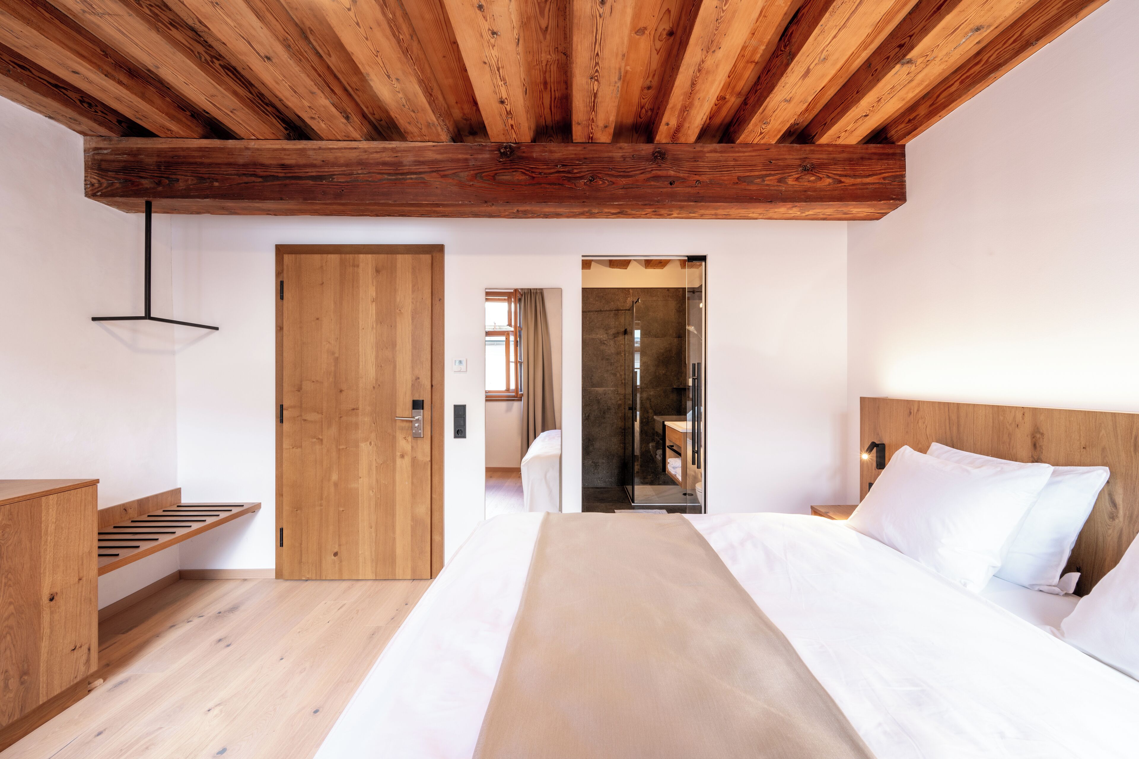 Une chambre avec un plafond en bois, un lit avec une literie blanche, une table de chevet en bois et un banc en bois.
