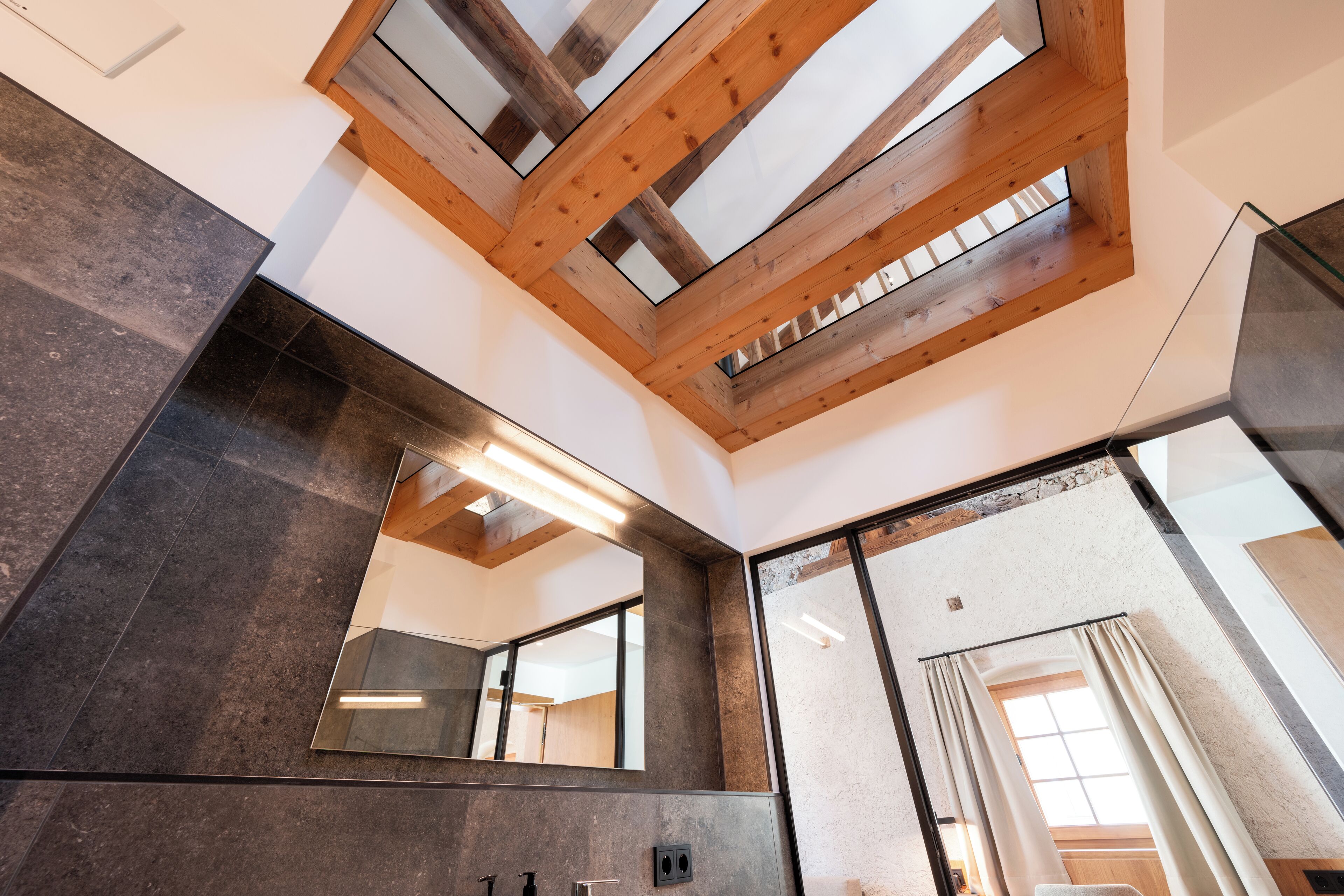 A modern bathroom with a skylight, large mirror, and dark tiles.