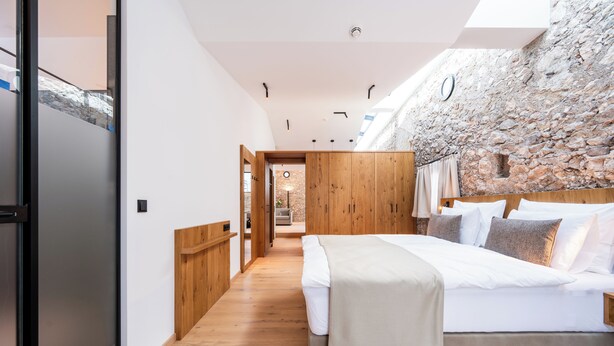A modern bedroom with a wooden bed, a stone wall, and a wooden floor. - Hotel Traube Rattenberg (Rattenberg)
