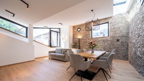 A modern dining area with a wooden table and chairs, a stone accent wall, and large windows offering views of the outdoors. - Hotel Traube Rattenberg (Rattenberg)