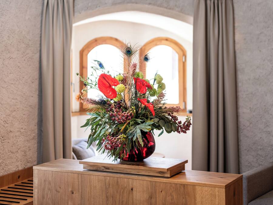 Una mesa de madera con un arreglo floral en una habitación rústica con vigas a la vista y paredes de piedra.