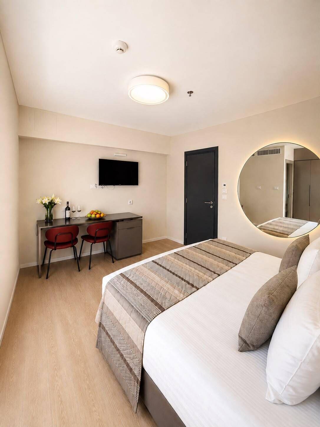 Habitación de hotel con cama, escritorio, dos sillas, televisor, puerta y espejo.