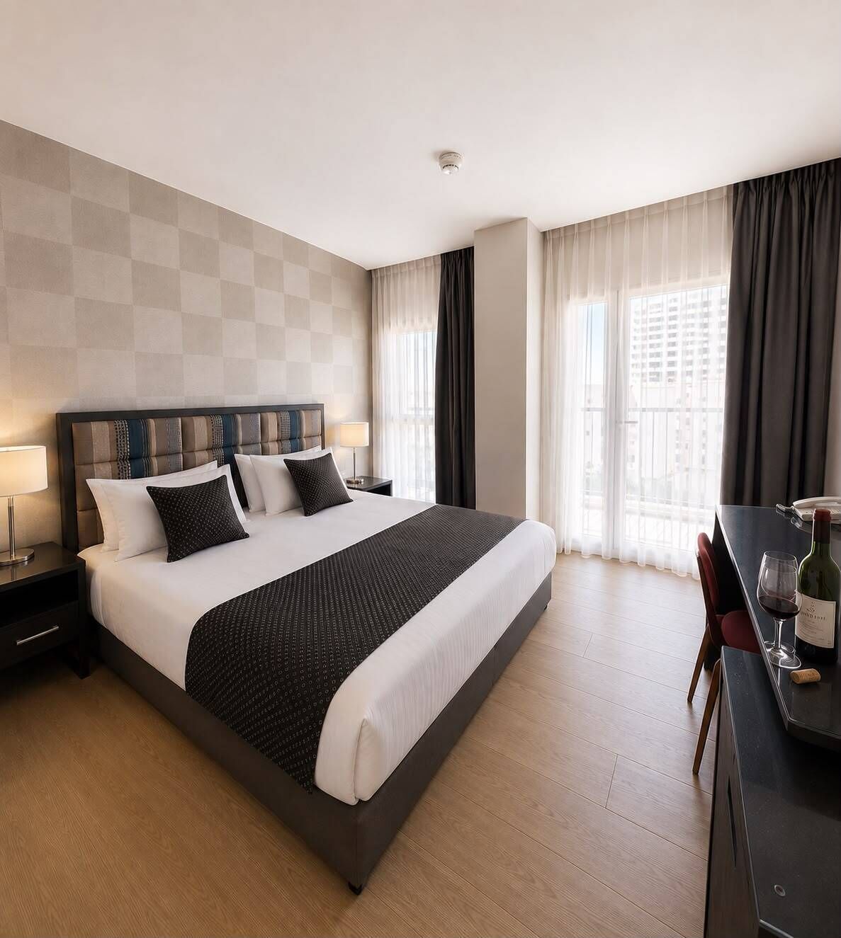 Ein Hotelzimmer mit einem großen Bett, einem Schreibtisch mit Stuhl, einer Lampe und einer Weinflasche.