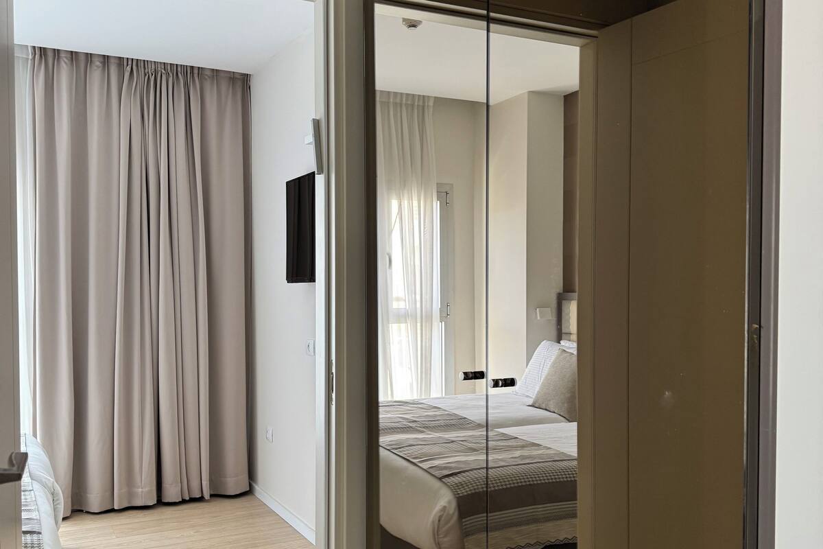 A modern bedroom with a large bed, a wardrobe, and a mirror.