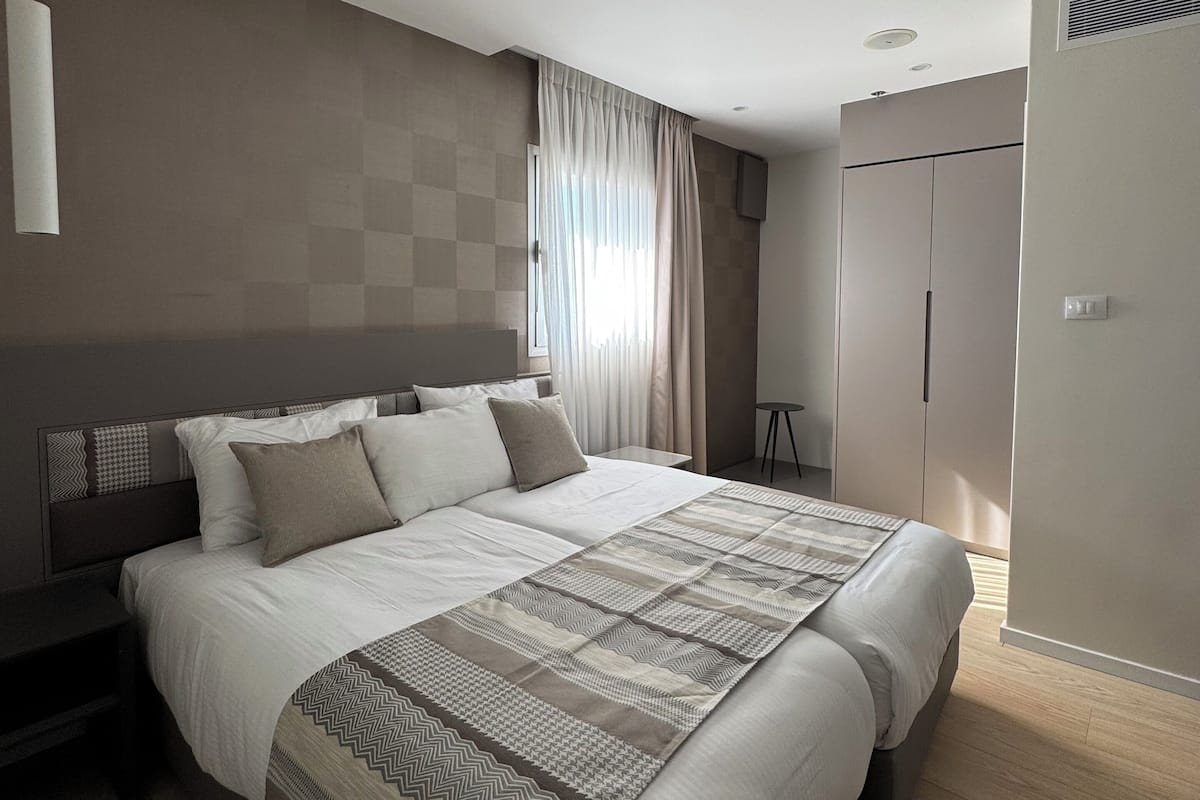 A modern bedroom with a large bed, a bedside table, a wardrobe, and a ceiling light.