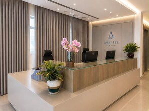A reception desk with a logo, two black chairs, a laptop, and a potted plant. - Abratel Sea View (Tel Aviv)