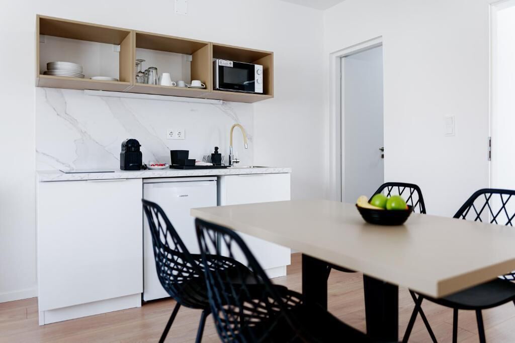 A modern kitchen with white cabinets, a microwave, and a coffee maker. There is a dining table with black chairs and a bowl of fruit.