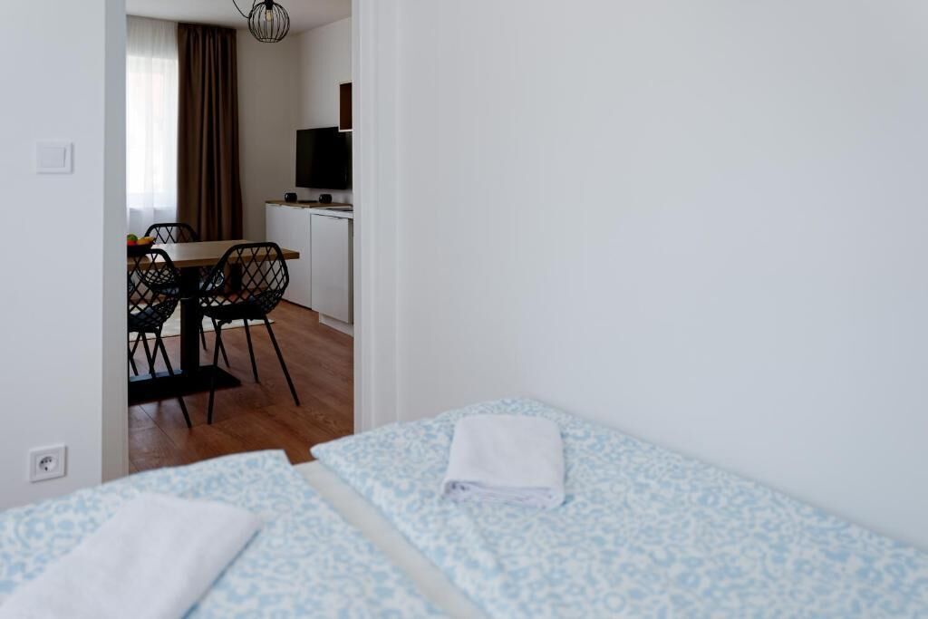 A hotel room with two beds, a small table with chairs, a TV, and a kitchenette in the background.