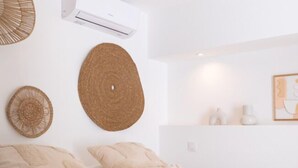 Un dormitorio con una cama, dos almohadones decorativos, un aire acondicionado de pared y un cuadro enmarcado.