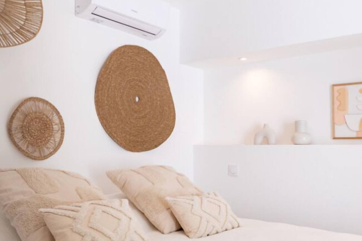 A bedroom with a bed, two decorative pillows, a wall-mounted air conditioner, and a framed picture.