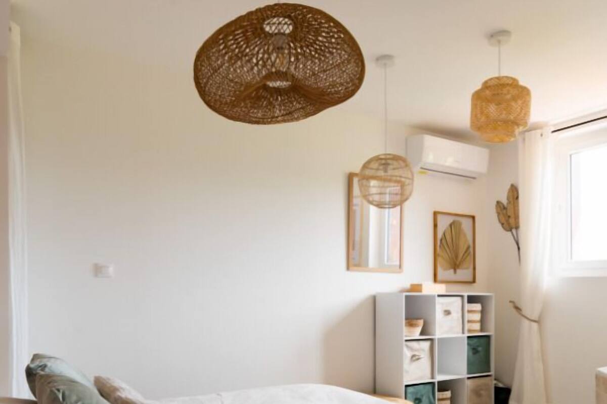 A bedroom with a bed, two pillows, a bedside table, a wall-mounted shelf with storage boxes, and two hanging light fixtures.