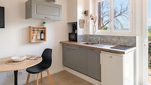 Una cocina compacta con comedor, que cuenta con horno integrado, un lavamanos y una ventana con vistas a árboles.