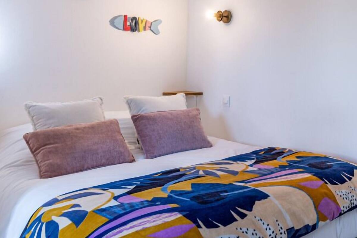 A bedroom with a bed, two pillows, a colorful blanket, and two wall decorations.
