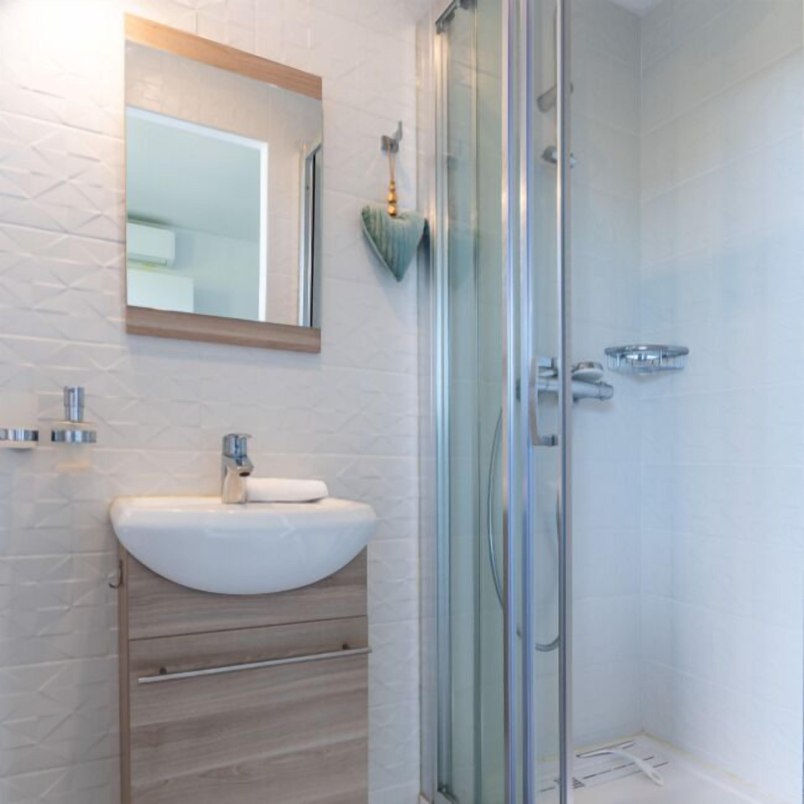 A modern bathroom with a white sink, wooden cabinet, and a glass shower enclosure.