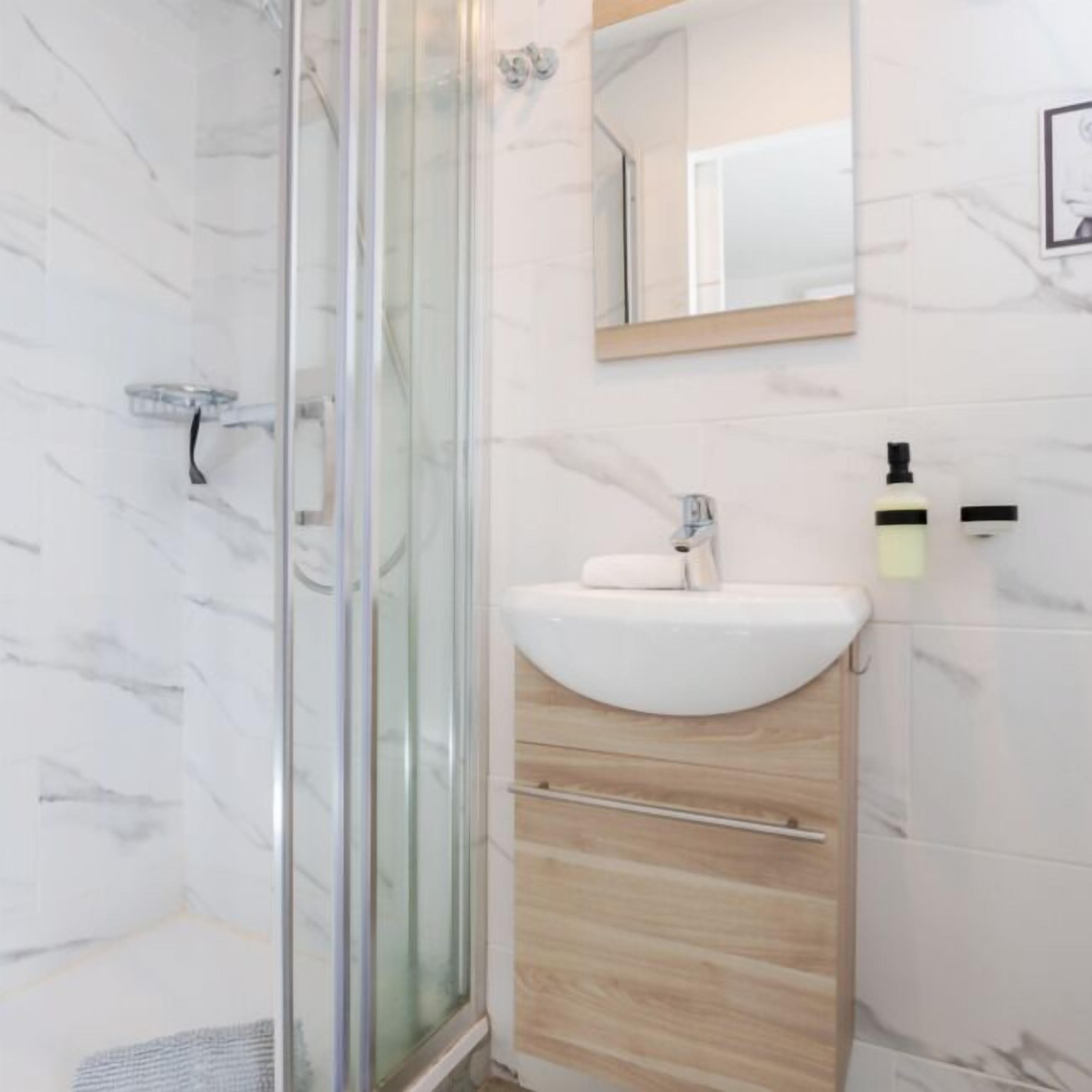 Une salle de bain moderne avec une douche à parois de verre, un lavabo blanc avec un meuble-vasque en bois et un miroir au-dessus du lavabo.