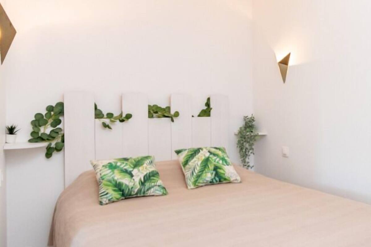 A bedroom with a bed, two pillows, a bedside plant, and wall-mounted sconces.