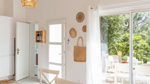Una habitación luminosa y espaciosa con una mesa de comedor lista para cuatro personas, un ventanal con vistas a zonas verdes y una lámpara colgante.