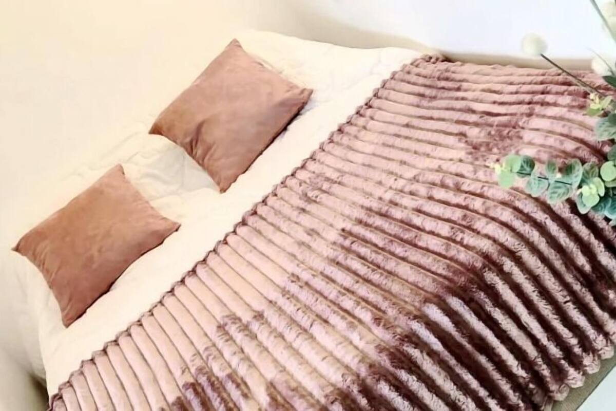 A bedroom with a bed, two pillows, a wall-mounted light fixture, and a decorative wall piece.