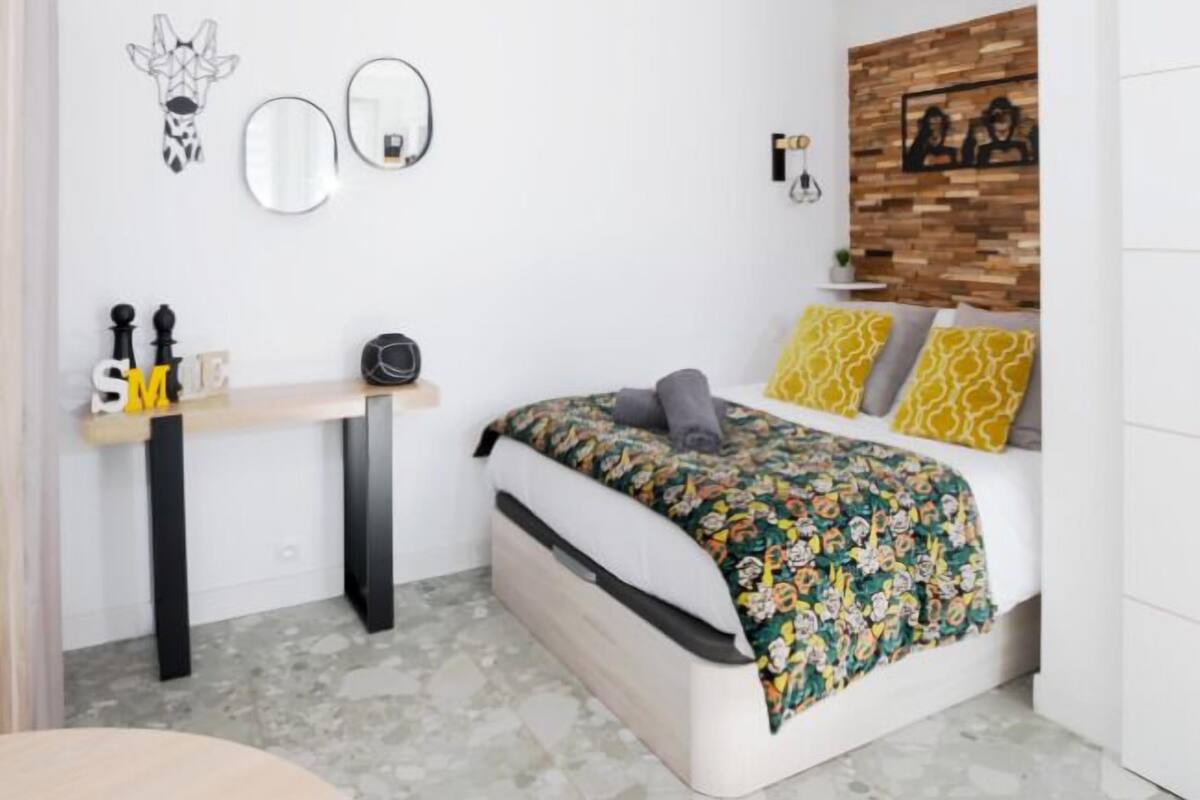 A bedroom with a bed, a desk, and a mirror.