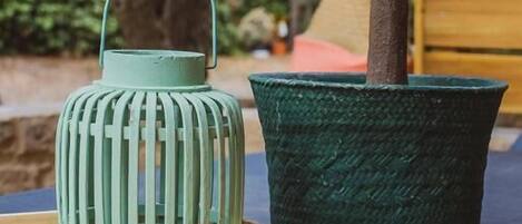 Una planta pequeña en maceta y un farol verde sobre una mesa de madera al aire libre.