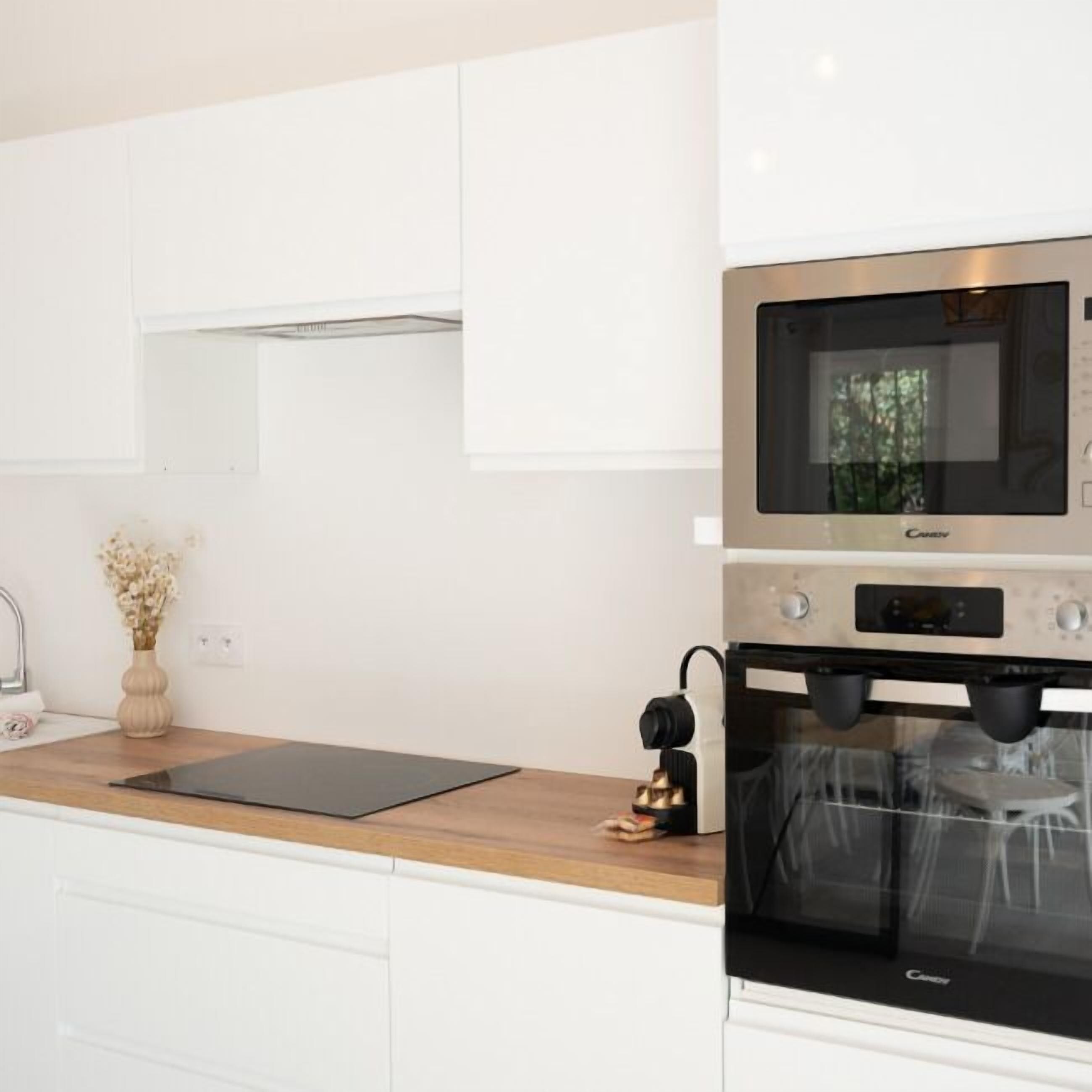 A modern kitchen with white cabinetry, a black countertop, a built-in oven, and a microwave.